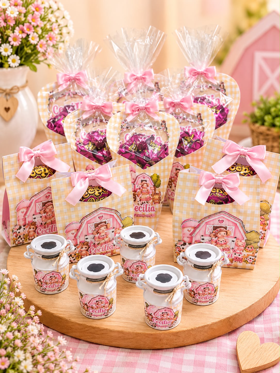Lembrancinhas personalizadas com tema fazendinha rosa: sacolinhas xadrez com laços de cetim rosa, cones transparentes com chocolates e mini latinhas de leite brancas, todas com o nome Cecília, sobre uma bandeja de madeira.
